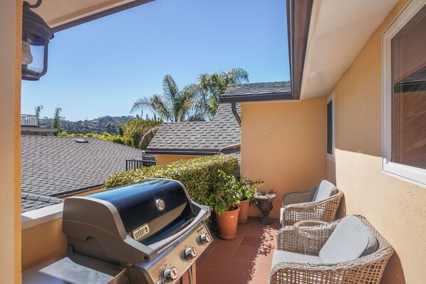 A balcony with a grill, wicker furniture, and potted plants.