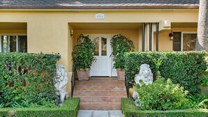 A building entrance with a tiled pathway leading to a white door, flanked by two stone lion statues and potted plants. - Affordable Beach Penthouse — 2 blocks to Beach and Funk Zone (Santa Barbara)