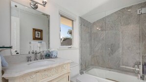 A bathroom with a marble shower, a sink with a mirror, and a toilet.
