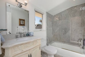 Een badkamer met een marmeren douche, een wastafel met spiegel en een toilet.