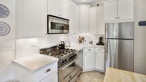 A modern kitchen with white cabinetry, stainless steel appliances, and a marble countertop.