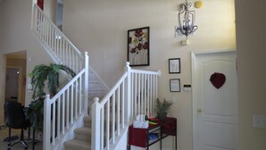 A staircase with white railings leading to an upper floor, a potted plant, a small table with a red cloth, and a door with a heart-shaped decoration. - 5 Star - 5 BR/4 Bath Villa - Perfect for Family vacation. Minutes to Disney. (Clermont)