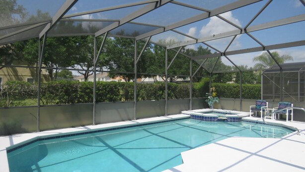 A covered outdoor swimming pool with a clear blue water feature, surrounded by a metal frame and a white deck. - 5 Star - 5 BR/4 Bath Villa - Perfect for Family vacation. Minutes to Disney. (Clermont)