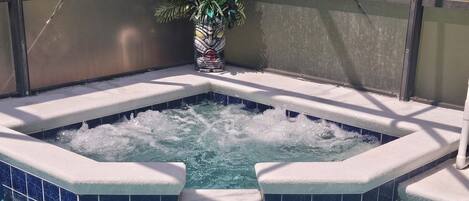 A hot tub with a tiled edge, surrounded by a pool.