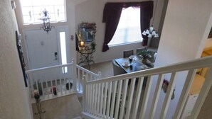 A staircase leading to a second-floor landing with a white railing, a chandelier, and a window with curtains. - 5 Star - 5 BR/4 Bath Villa - Perfect for Family vacation. Minutes to Disney. (Clermont)