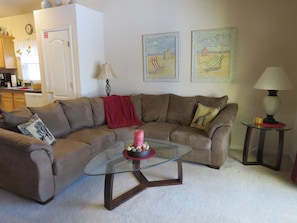 A living room with a brown sectional sofa, a glass coffee table, and two framed beach paintings on the wall.