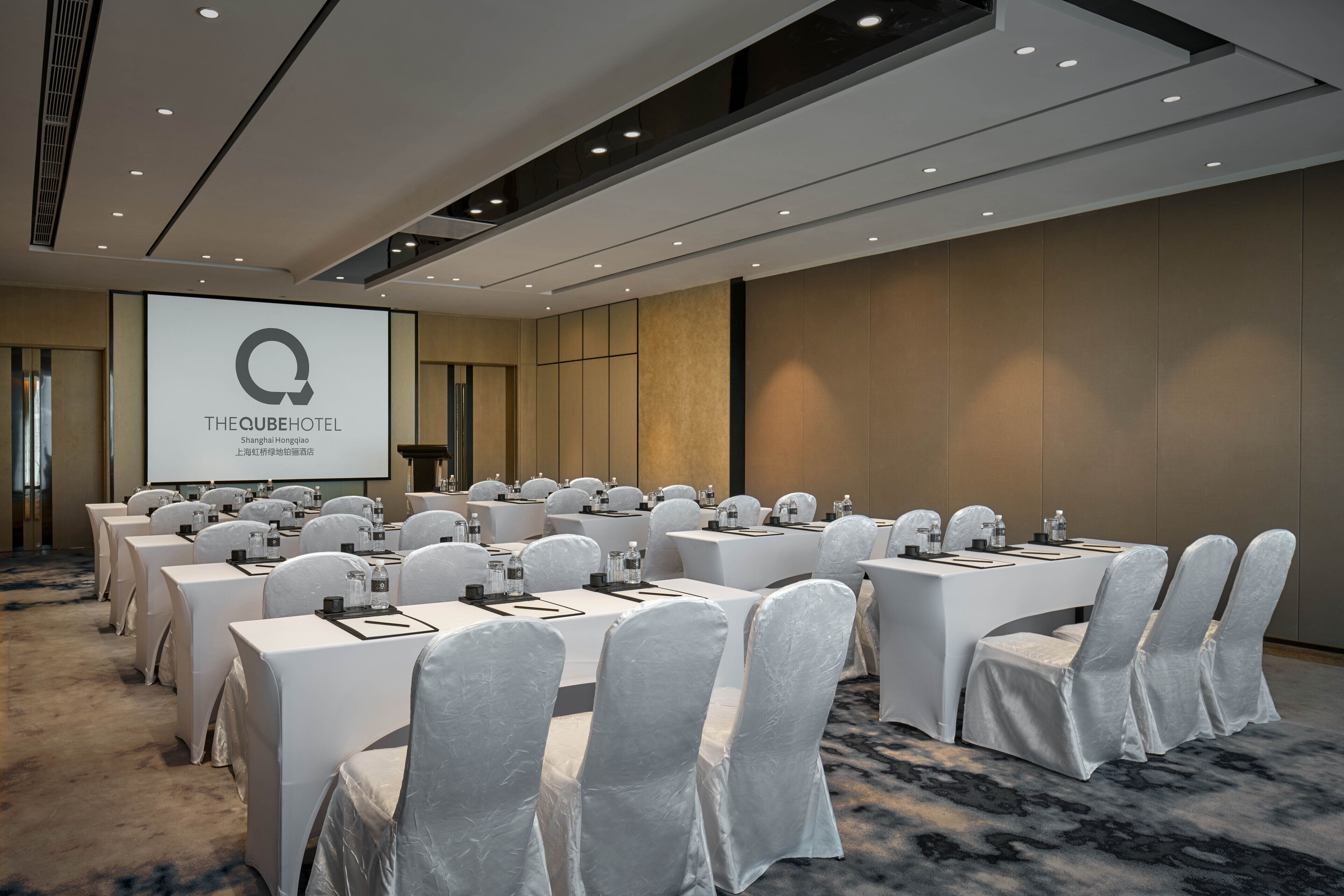 A conference room at The Cube Hotel with multiple tables, chairs, and a presentation screen.