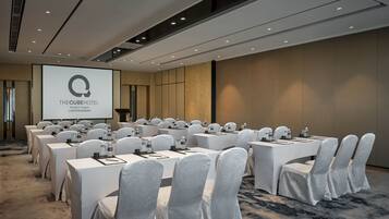 A conference room at The Cube Hotel with multiple tables, chairs, and a presentation screen.