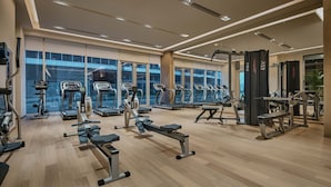 A modern gym with various exercise equipment, large windows, and a clean, spacious layout.