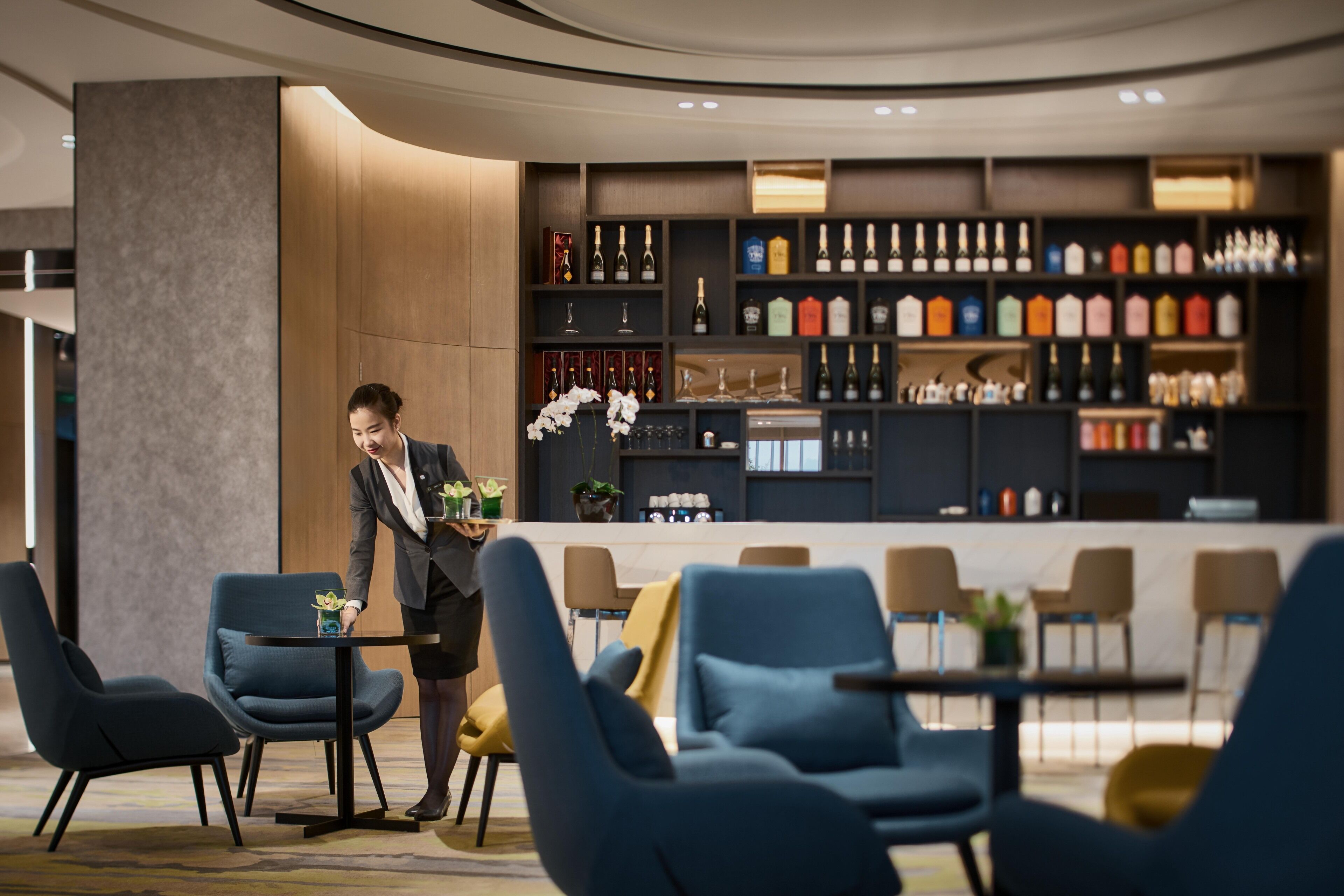 A modern hotel lobby with a bar area, seating, and a person arranging flowers.