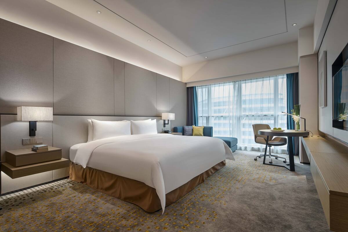 Een moderne hotelkamer met een groot bed, nachtkastjes, een bureau en uitzicht op de stad.