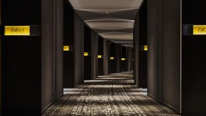 A long, narrow hallway with dark walls and a patterned carpet. There are illuminated signs with numbers on the walls, indicating room numbers.