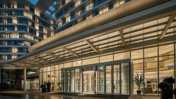 A modern hotel with a curved facade, large glass entrance, and multiple balconies.