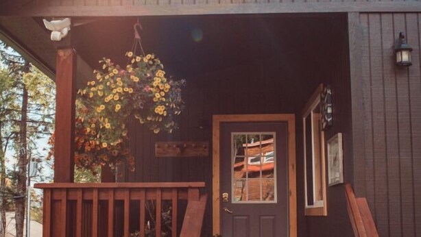 A wooden building with a porch, a door, and a hanging flower basket.