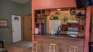A compact kitchen with a central island, wooden stools, and a refrigerator.