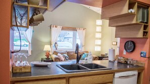 A compact kitchen with a sink, a dishwasher, and a window with curtains.