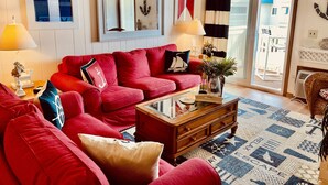 A living room with a red sofa, a coffee table, and a view of the outside through a sliding glass door.