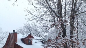 Una cabaña de madera con techo nevado, chimenea y porche.
