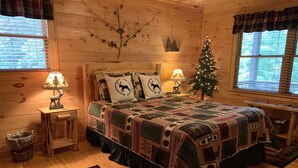 Un dormitorio rústico de cabaña con una cama grande, dos lámparas de noche, un árbol de Navidad y un adorno en la pared.