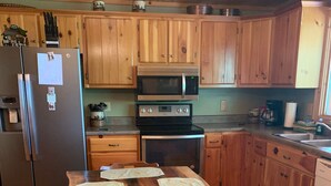 Una cocina con armarios de madera, un refrigerador de acero inoxidable, un microondas, una estufa y una mesa de comedor de madera con tortillas.