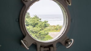 A round window with a view of the ocean and greenery.
