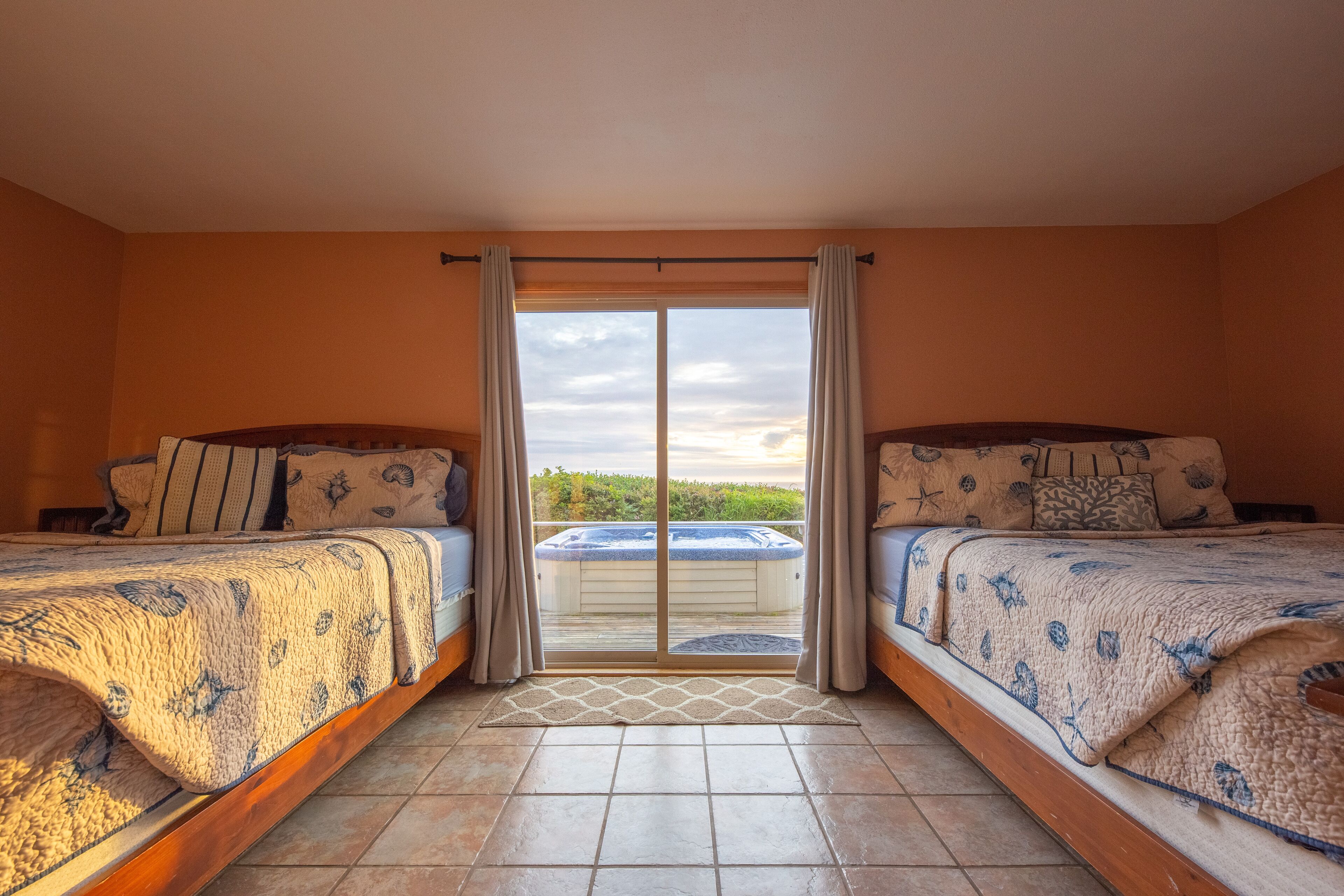 A bedroom with two beds, a sliding glass door leading to a balcony, and a hot tub visible through the door.