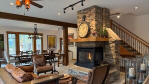 Un salón amplio con chimenea de piedra, mobiliario de cuero y una escalera que conduce a un nivel superior.