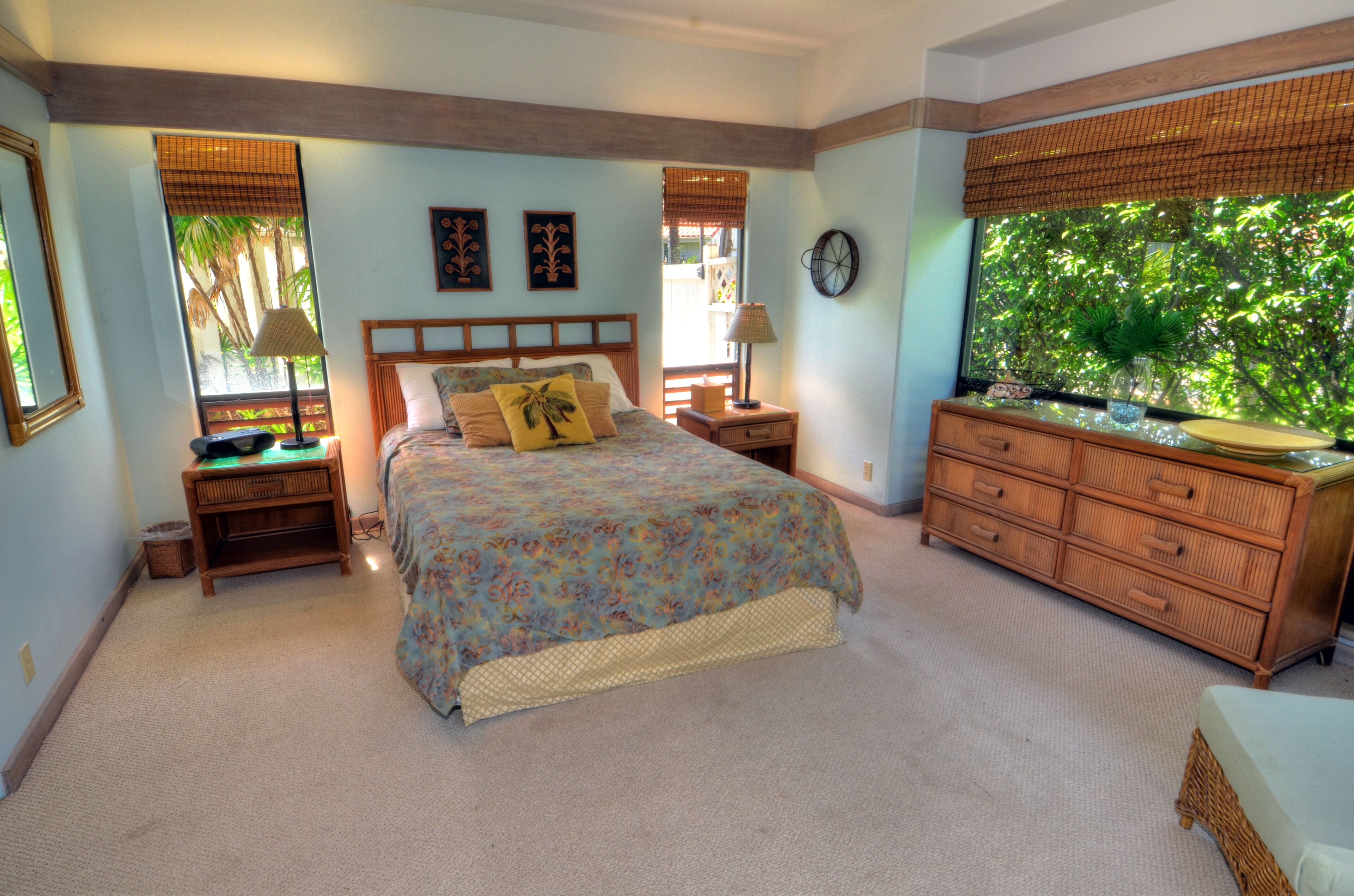 A bedroom with a bed, nightstands, a dresser, and a large window with a view of trees.