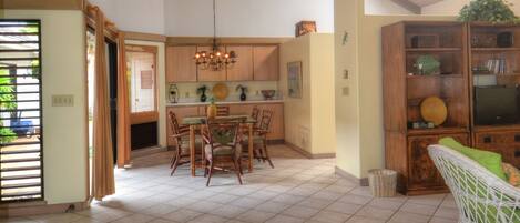 A spacious living area with a high ceiling, a dining table, and a seating area with cushions.