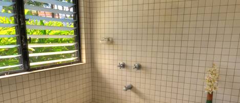 Een badkamer met een ruim bad, een raam met zonwering en een kleine vaas met bloemen.