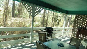 A covered outdoor area with a table and chairs, a grill, and a view of a forested area. - A Short Walk to Dauphin Island Beach.*Pets Welcome* 
special rates 20% Discount  (Dauphin Island)