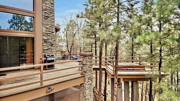 A modern cabin with a stone exterior, wooden deck, and a view of surrounding pine trees. - Timberloft Luxury Lodge, HOT TUB , GOLF COURSE views, secluded & private (Flagstaff)