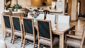 A spacious dining area with a high ceiling, wooden dining table, and chairs, connected to a kitchen area with wooden cabinets and a stone backsplash. - Timberloft Luxury Lodge, HOT TUB , GOLF COURSE views, secluded & private (Flagstaff)