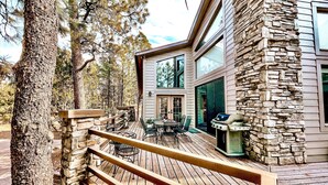Una casa moderna con fachada de piedra, una terraza de madera y un patio amueblado.