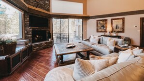 A spacious living room with a stone fireplace, a large sofa, and a dining area. - Timberloft Luxury Lodge, HOT TUB , GOLF COURSE views, secluded & private (Flagstaff)