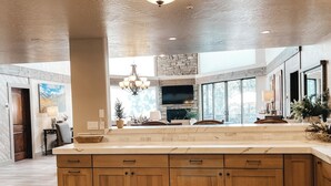 A spacious kitchen with wooden cabinets, a large island, a stone accent wall, and a chandelier. - Timberloft Luxury Lodge, HOT TUB , GOLF COURSE views, secluded & private (Flagstaff)