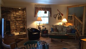 A cozy living room with a stone fireplace, a wooden dining table, and a comfortable sofa.