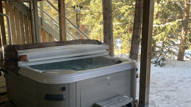 A hot tub with a wooden deck and a metal railing, surrounded by trees and snow.