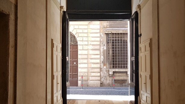 A corridor with a herringbone floor leading to an open doorway. - Residenza Sinibaldi - XVI century experience (Rome)