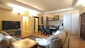 A living room with a sofa, a TV, a dining area with chairs, and a kitchen in the background. - Residenza Sinibaldi - XVI century experience (Rome)