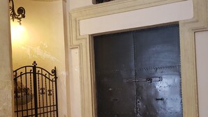 A large, dark metal door with a simple latch mechanism, flanked by white walls and a wooden floor. - Residenza Sinibaldi - XVI century experience (Rome)
