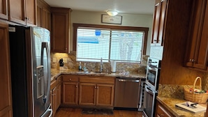 Una cocina con armarios de madera, electrodomésticos de acero inoxidable, encimera de granito y una ventana con persianas.