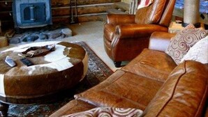 A log cabin interior with a fireplace, leather furniture, and a mounted deer head. - WindRiver/ Yellowstone Cabin (Dubois)