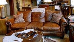 A rustic cabin interior with a wooden staircase, a leather sofa, a round ottoman, and a patterned rug. - WindRiver/ Yellowstone Cabin (Dubois)