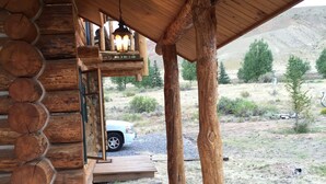 A wooden log cabin with a covered porch, a car parked outside, and a mountainous landscape in the background. - WindRiver/ Yellowstone Cabin (Dubois)