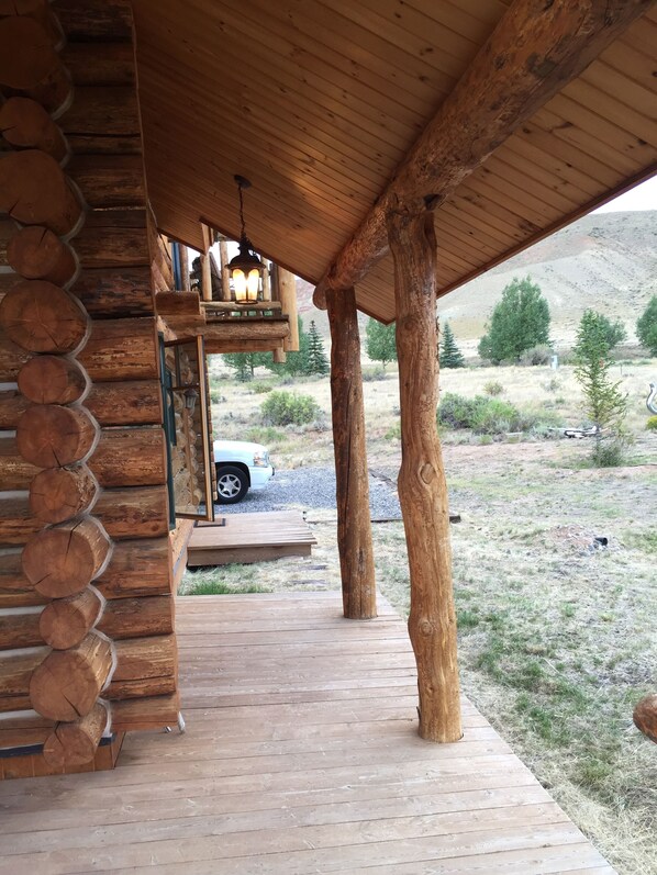 A wooden log cabin with a covered porch, a car parked outside, and a mountainous landscape in the background.