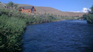 A log cabin by a river with a clear view of the surrounding landscape. - WindRiver/ Yellowstone Cabin (Dubois)