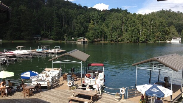 A docked boat area with wooden benches and tables, surrounded by water and forested hills.