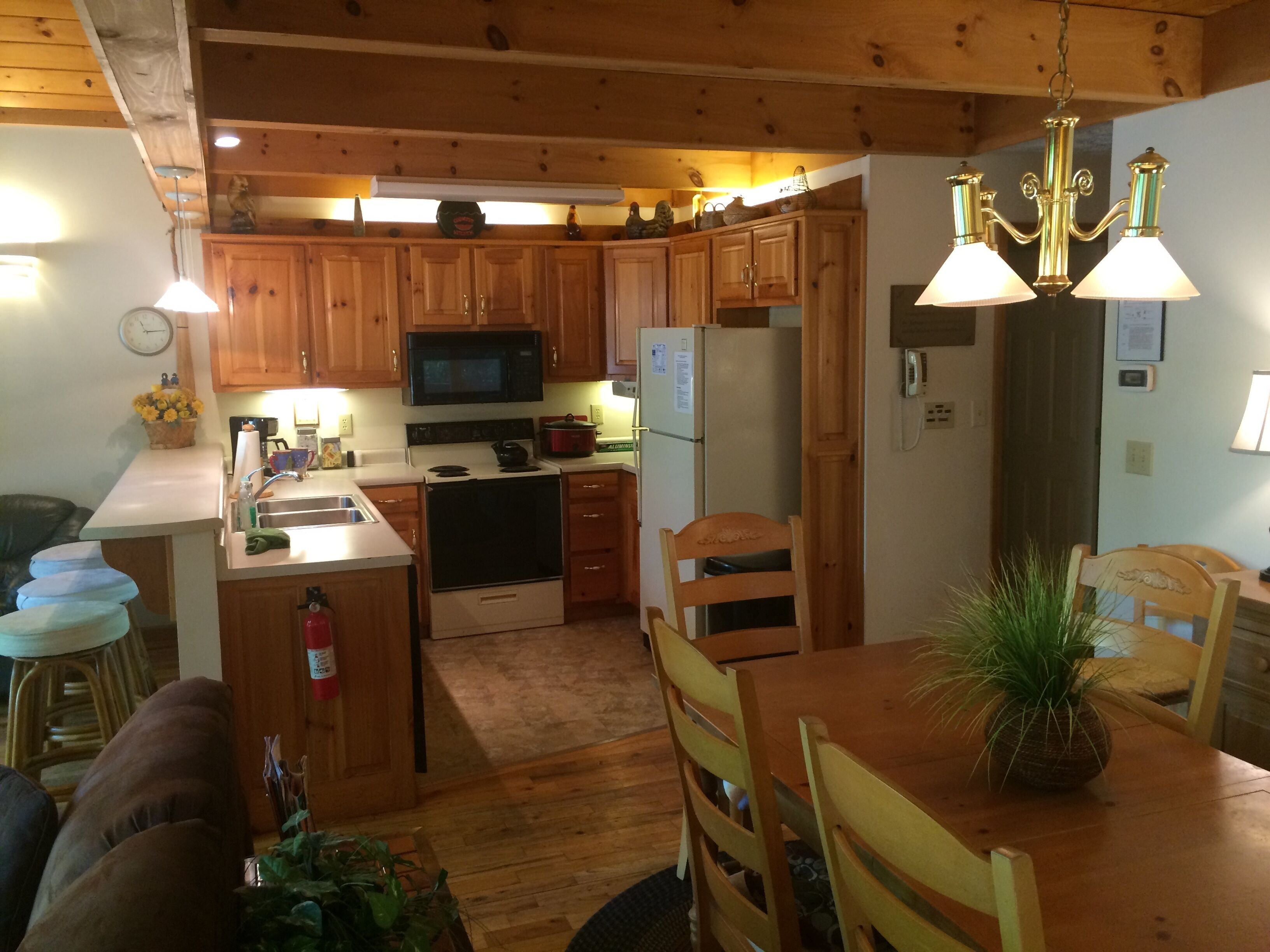 A kitchen with wooden cabinets, a microwave, stove, refrigerator, and a dining area with a table and chairs.