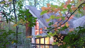 A cabin with a deck and a large window, surrounded by trees.